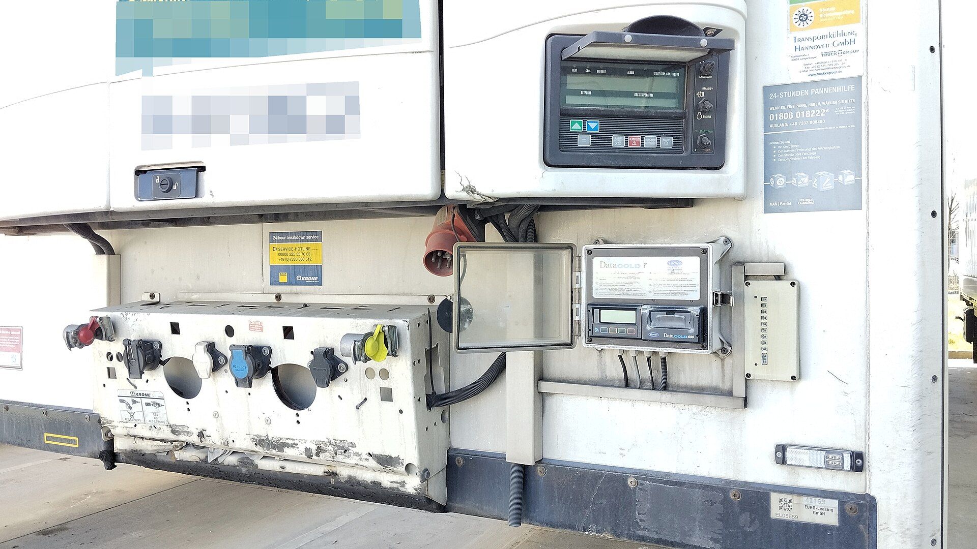 Open weatherproof enclosure on the front bulkhead of a refrigerated semi-trailer holding a temperature recorder with a ticket printer, beside the refrigeration unit's control panel