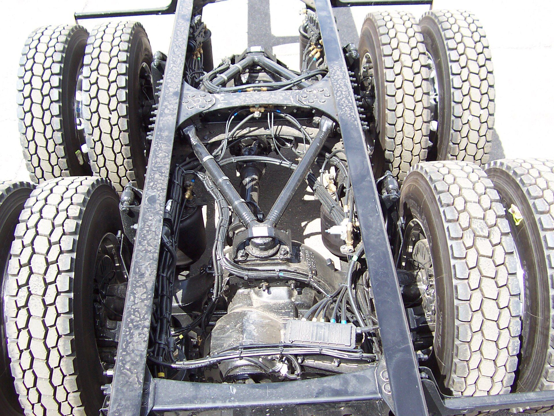 Rear tandem bogie of a 6x4 chassis seen from above between the frame rails, propeller shaft and universal joint running between the two drive axles