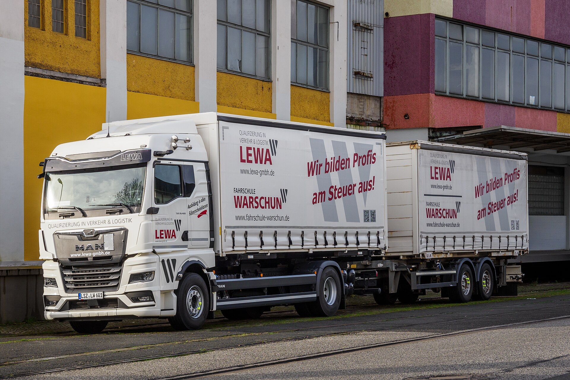 MAN TGX rigid truck and drawbar trailer in driving-school livery parked beside an industrial building in Bremen