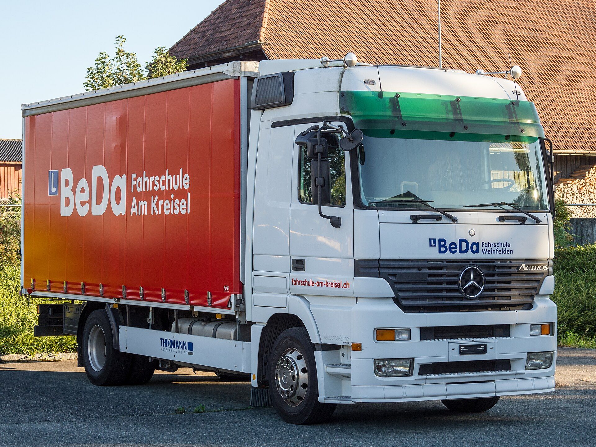 Mercedes-Benz Actros curtainsider rigid in driving school livery, carrying an L plate, parked at Bürglen in Switzerland