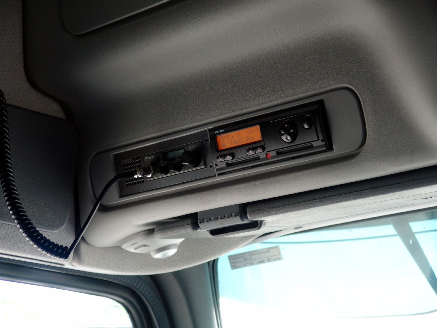 Volvo-branded digital tachograph with two driver card slots in the overhead console of a truck cab, beside a CB radio