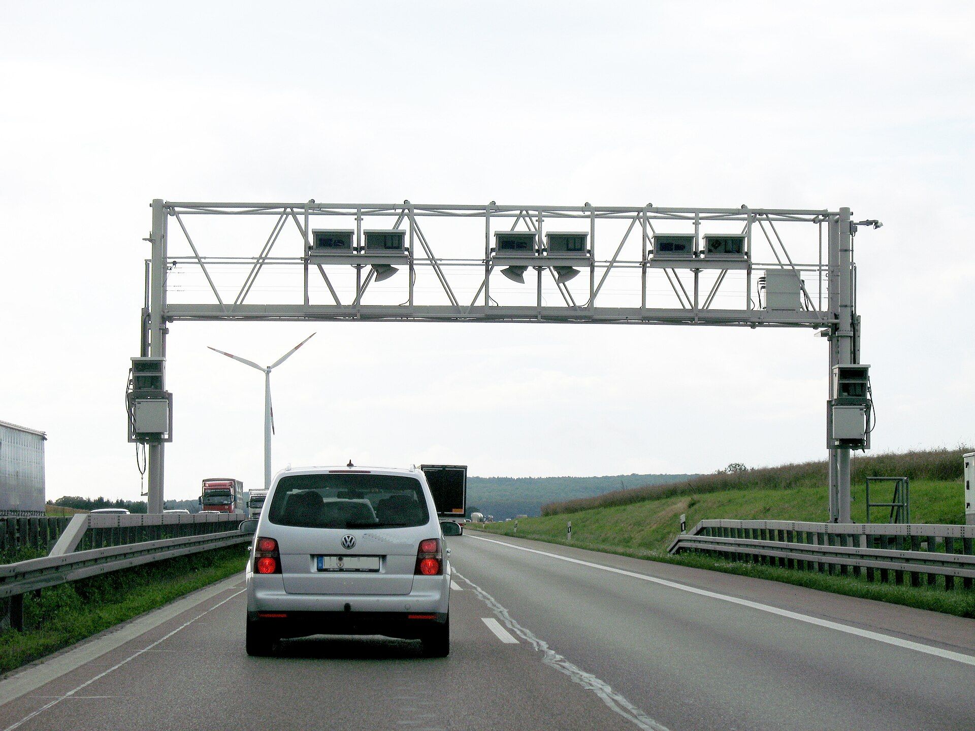Toll Collect enforcement gantry spanning a German Autobahn carriageway, with lorries approaching in the left-hand lane