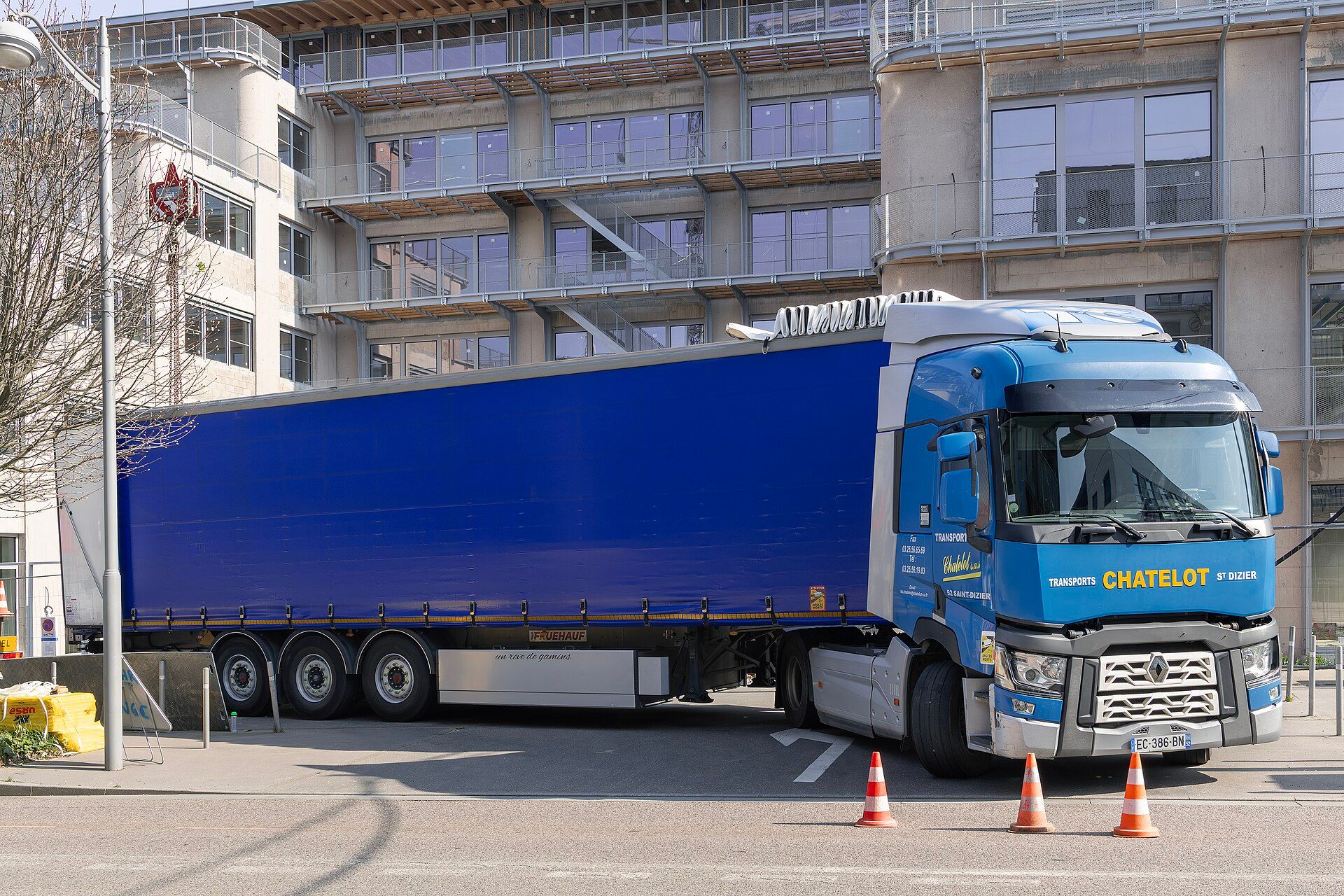 Blue Renault Trucks T two-axle tractor unit in its pre-2021 form — chrome grille bars, solid chrome diamond and separate headlamps — coupled to a curtainside semi-trailer at a city kerbside