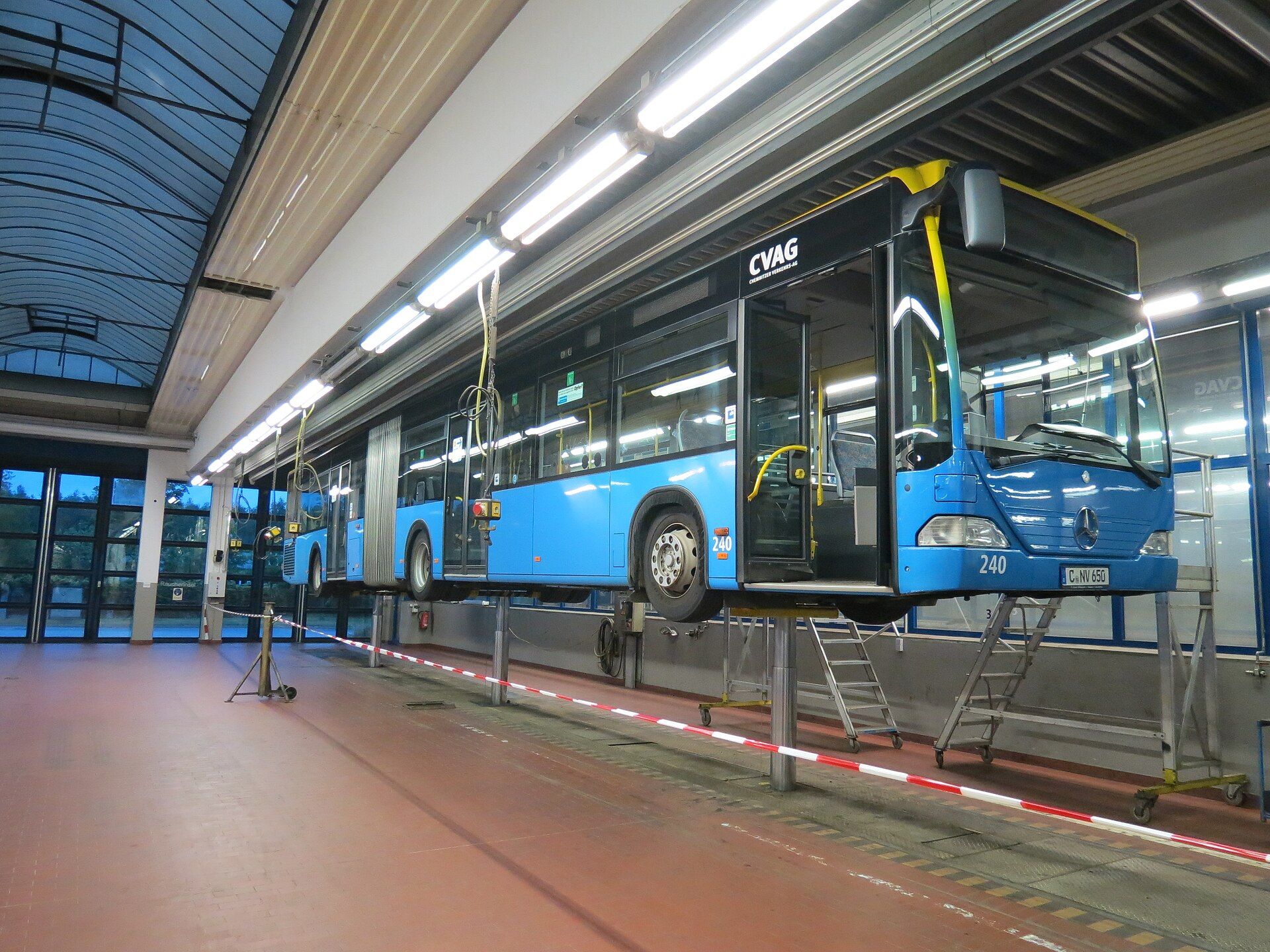 Articulated city bus raised on column lifts inside the workshop hall of a municipal bus depot