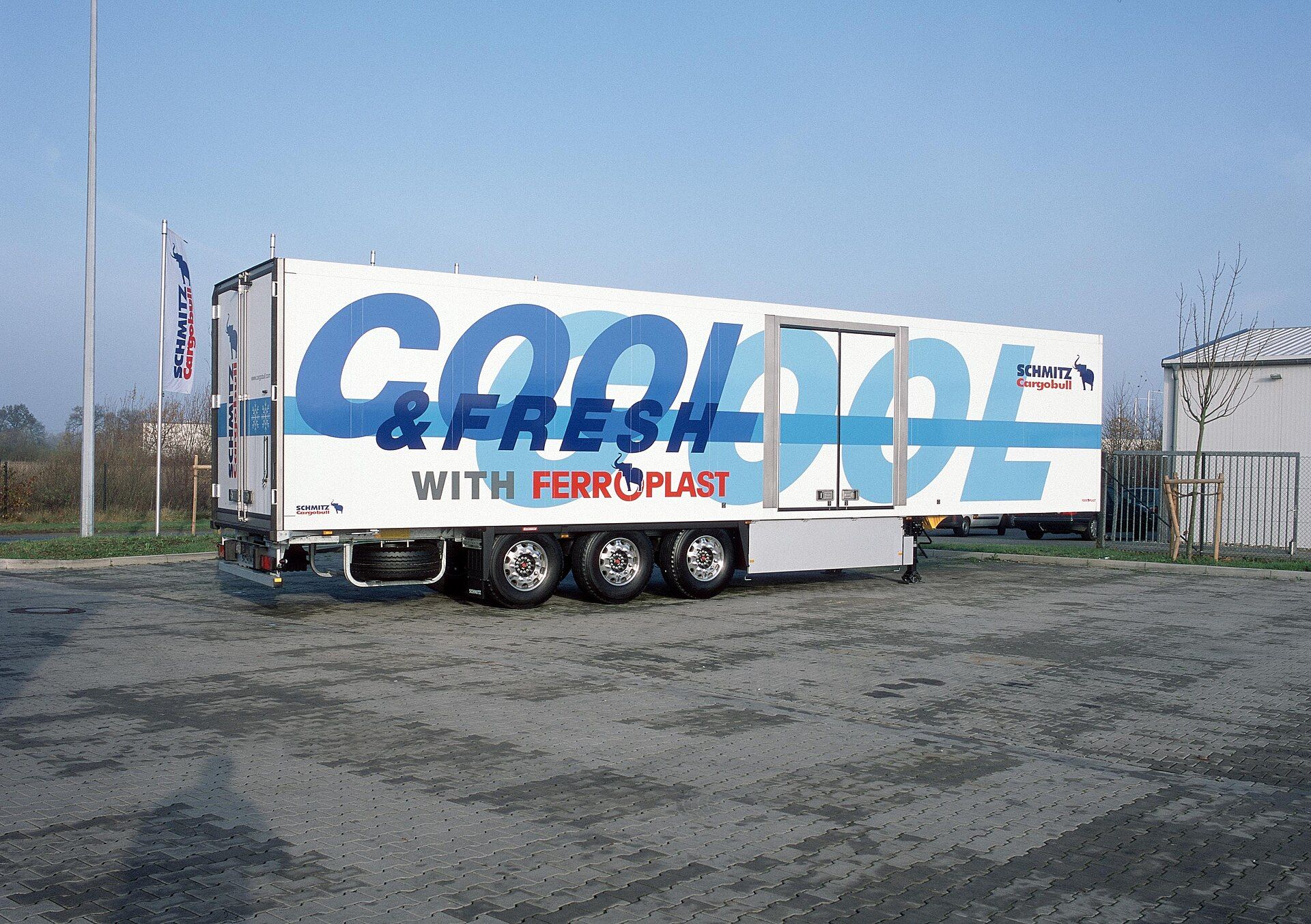 Uncoupled three-axle Schmitz Cargobull insulated box semi-trailer with a side door, standing on its landing legs in the maker's Cool and Fresh FERROPLAST demonstration livery
