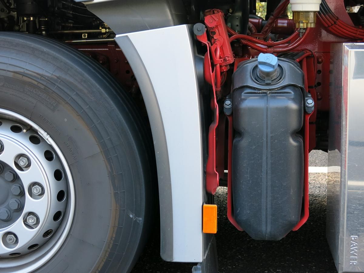 AdBlue tank with its blue filler cap on a red truck chassis, between the road wheel and an aluminium side box embossed Bawer
