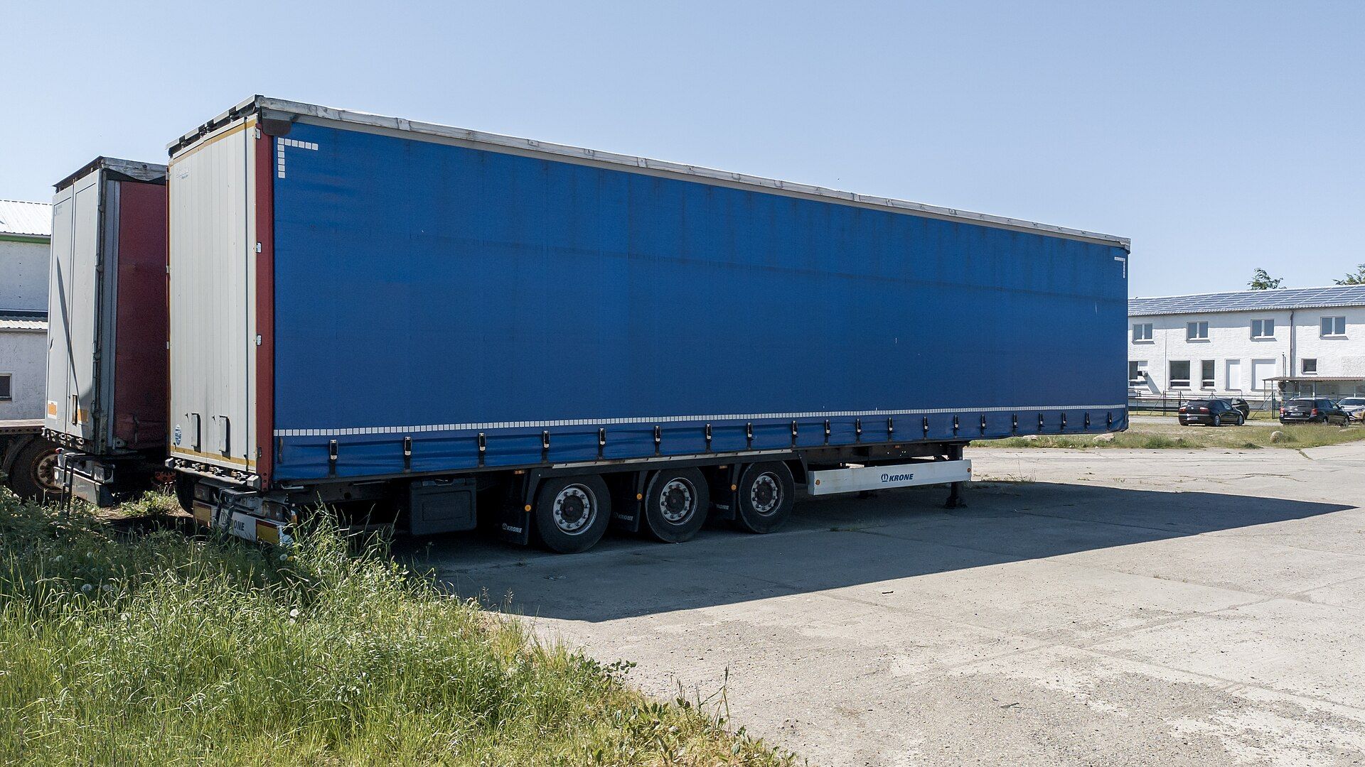 Uncoupled Krone three-axle curtainside semi-trailer standing on its landing legs in a yard