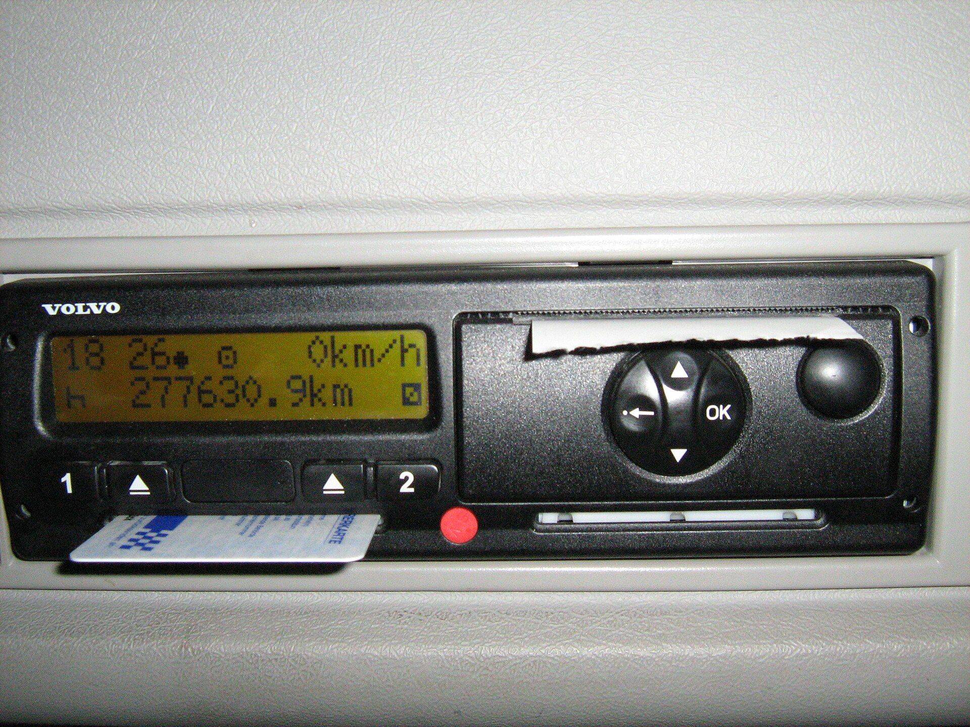Digital tachograph head in a truck dashboard, driver card inserted in slot 1 and printer paper protruding from the slot