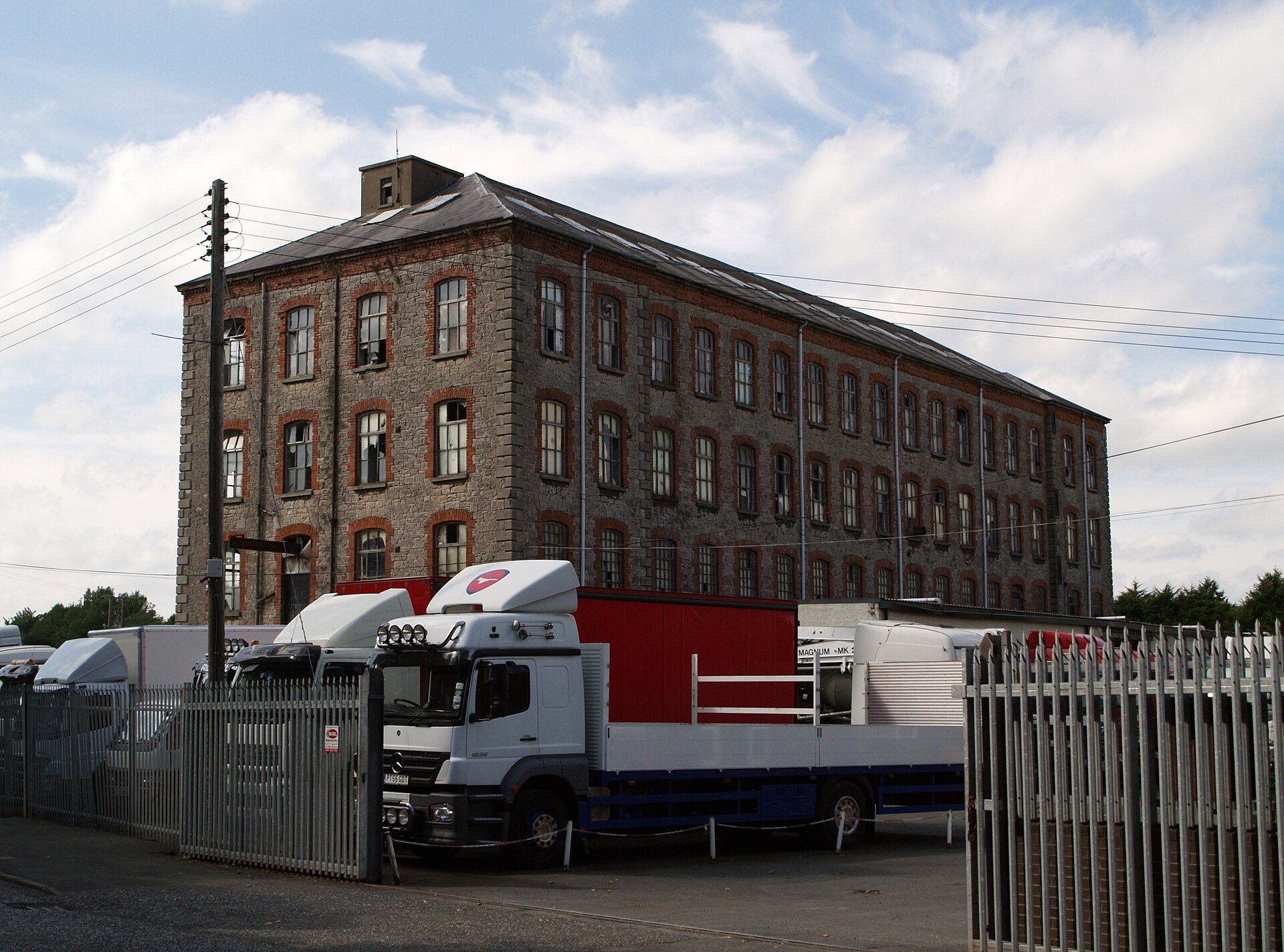 Used lorries and tractor units parked behind palisade fencing in a sales yard beside a disused mill in Armagh