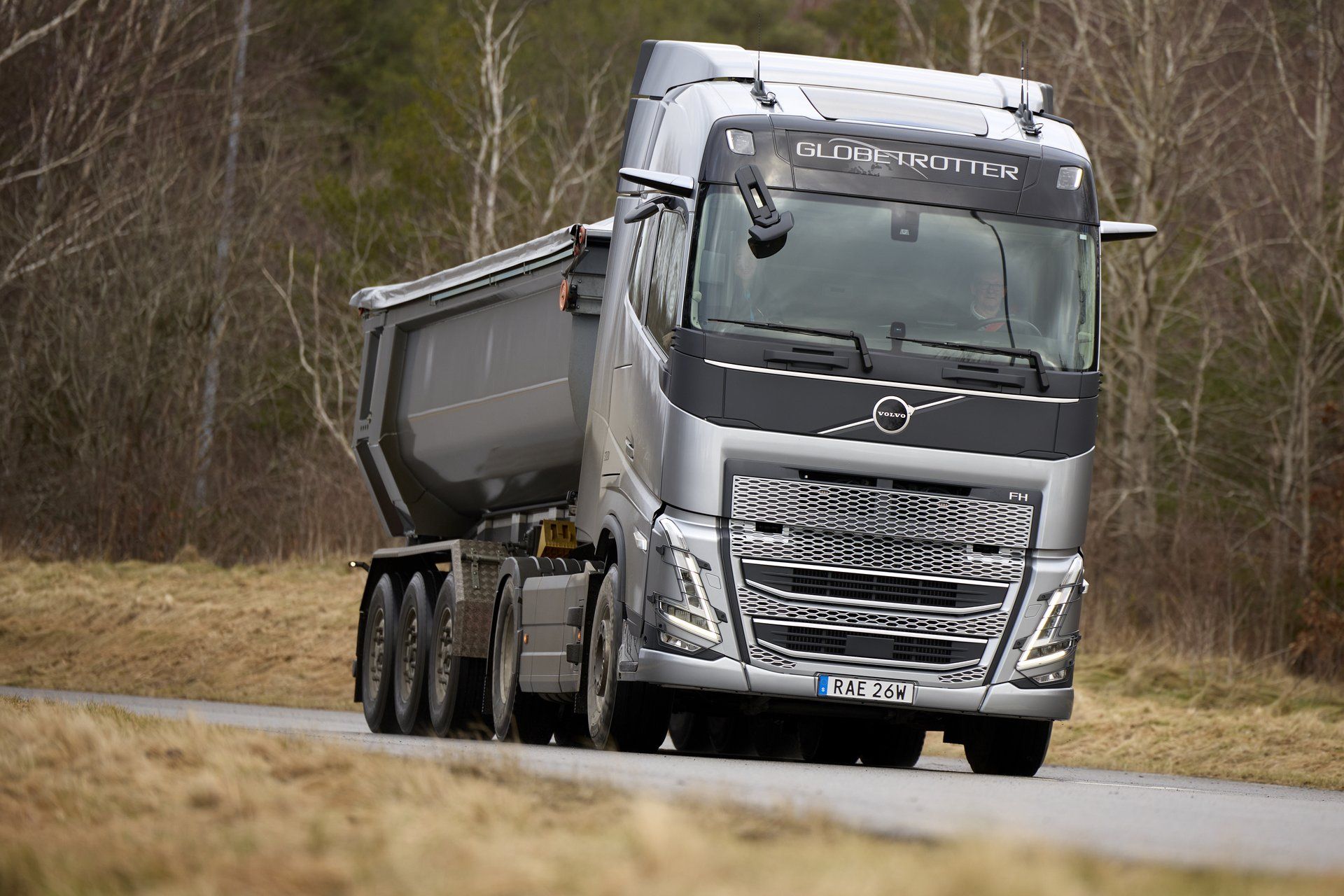 Globetrotter kabinli, 2020 neslinden gümüş renkli iki dingilli Volvo FH çekici, üç dingilli damperli yarı römorkla kışın yaprakları dökülmüş bir ormanın içinden geçen yolda