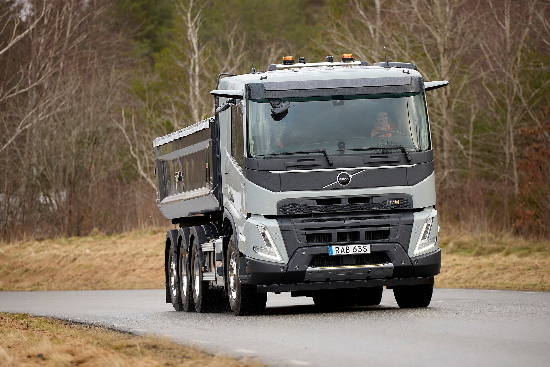 White Volvo FMX four-axle tipper with a single steering front axle and a rear tri-axle group, on a rural road